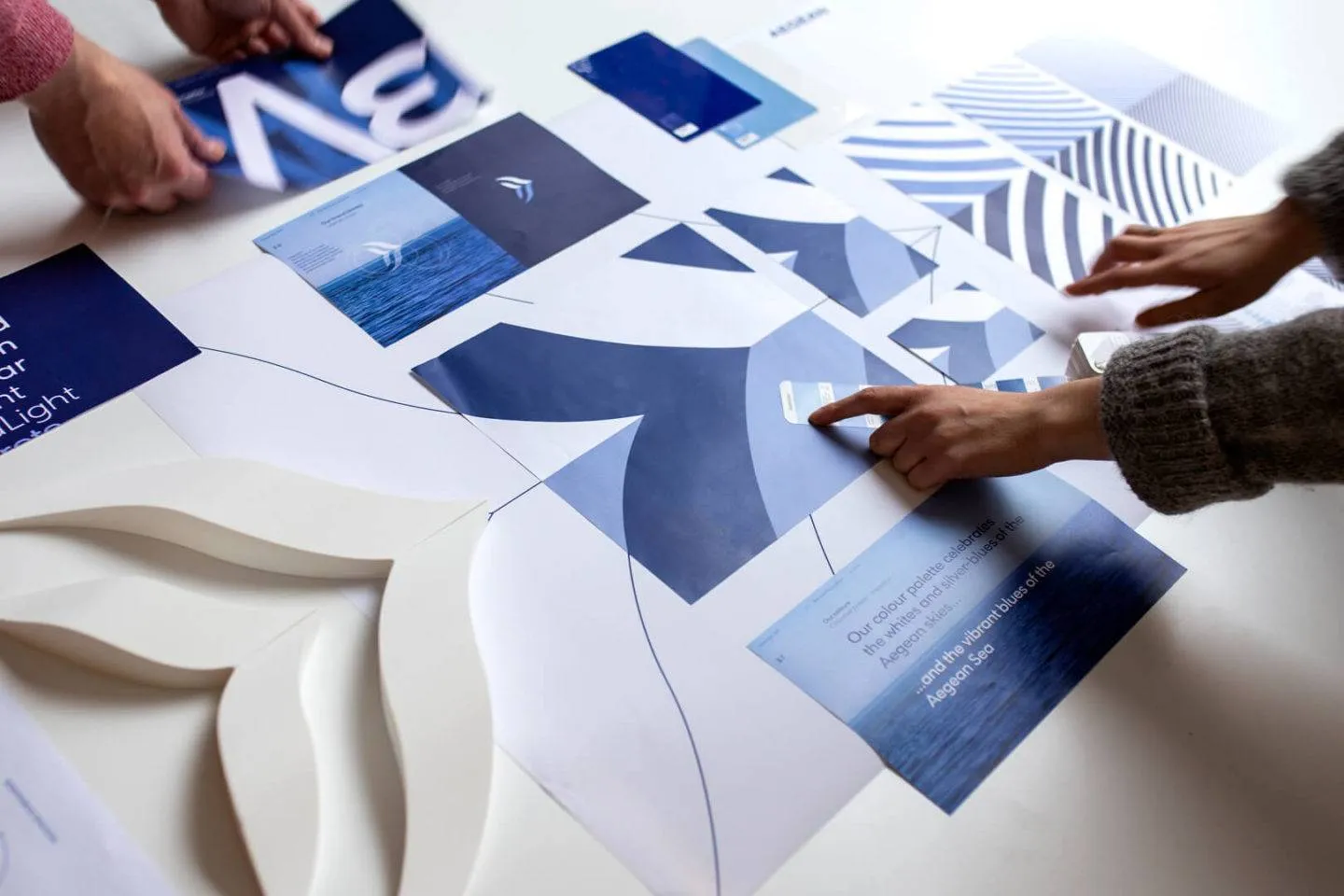 Hands pointing at different print outs laid out, showing the new Aegean Airlines brand elements, including logo, patterns and colours