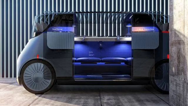 Side view of a vehicle with open doors, showing sofa like seating in the interiors, soft lighting, set against a slatted architectural background