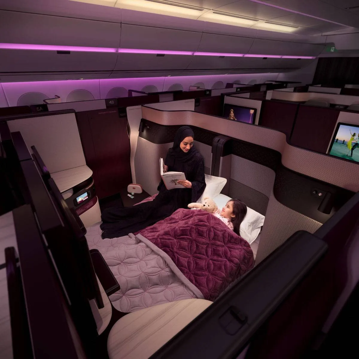 A woman reads to her daughter in the double bed configuration of the QSuite. A removable panel allows two center seats to come together to form one large double bed