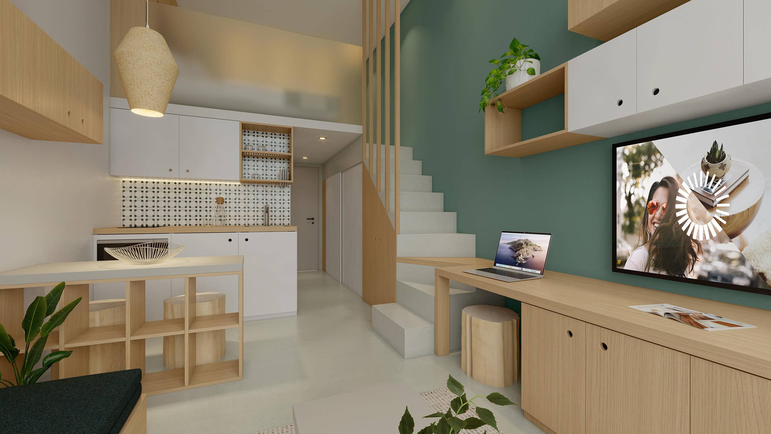 A light residential interior space, with a kitchen and dining table on the left, a long desk, shelving units and TV on the right. On the right is also a staircase leading up to a mezzanine room
