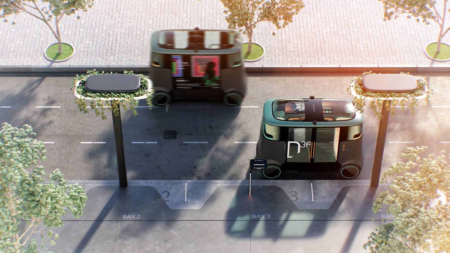Two Dromos autonomous vehicles seen from above. The vehicles are on a road, which features three narrow lanes. Greenery surrounds the Dromos stops and the pavement alongside the vehicles' route