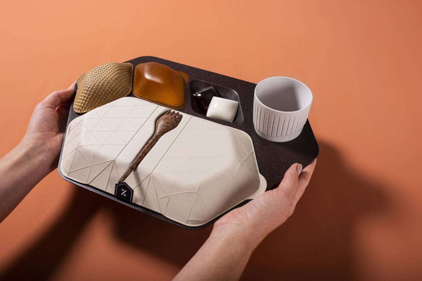 Two hands holding an airline meal tray made from sustainable materials including wafer biscuit, algae, coconut wood and ground coffee