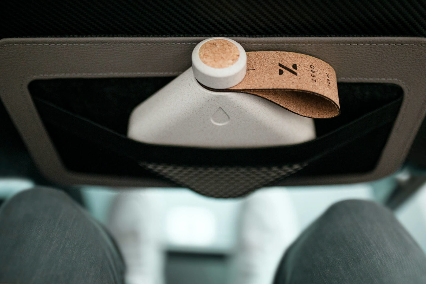 A square water bottle shown in the seat back pocket of an airline seat