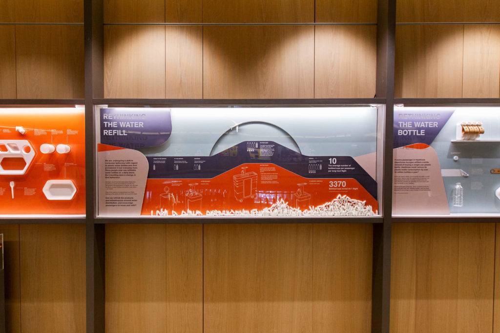 Exhibition view of Get Onboard at the Design Museum, with display cases on the wall. Two blurred people can be seen looking at the displays