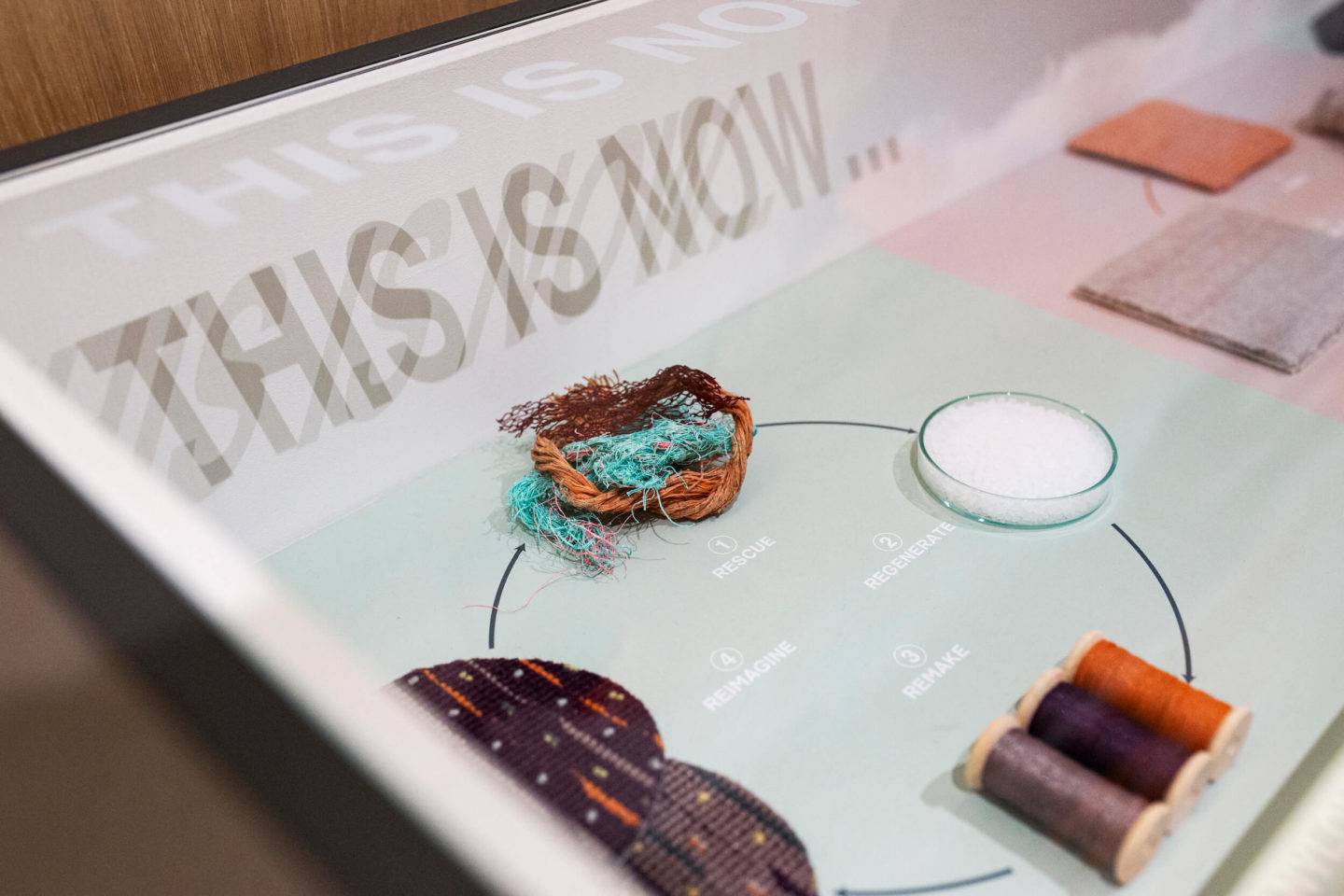 This is now. Detail view of a display case in an exhibition showing circular design of carpet made from fishing net