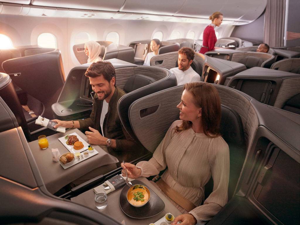 Business class cabin showing passengers enjoy the meal service, while a cabin crew serves a passenger