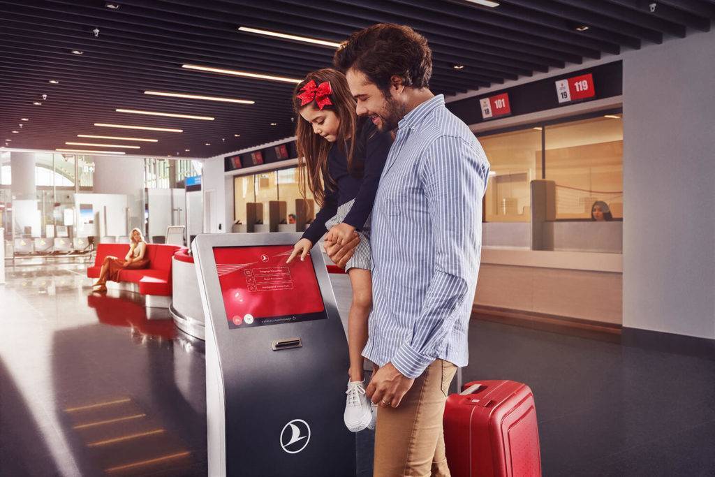A man holding his young daughter in his arms as she touches the screen of a Turkish Airlines ticket machine