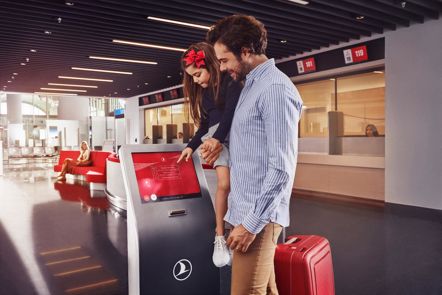 A man holding his young daughter in his arms as she touches the screen of a Turkish Airlines ticket machine