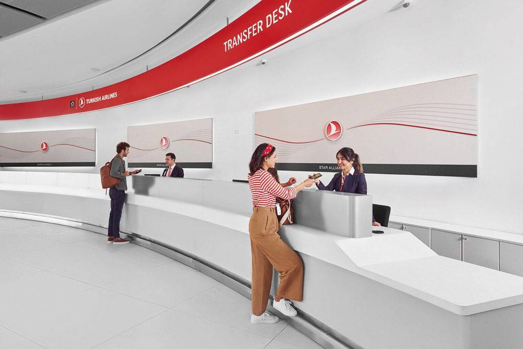 Turkish Airlines transfer desk at New Istanbul Airport. Two passengers are each speaking to a Turkish Airlines employee behind a long desk