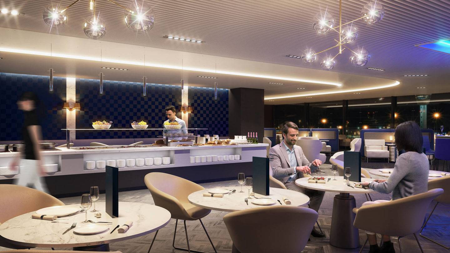 Two passengers seated at a table eating in the luxurious Polaris airport lounge. In the background is a large buffet area, with a person stood on the other side of the buffet