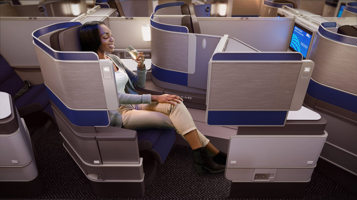 A woman is drinking champagne seated in a Business Class aircraft seat