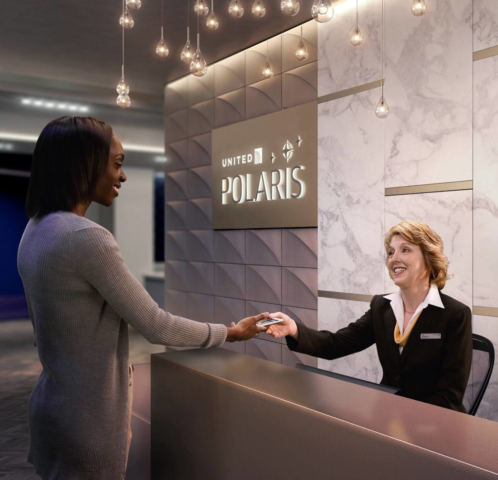 A passenger is greeted by a receptionist at the entrance to the United Polaris lounge. A marbled wall and 3D branded panel feature in the backdrop