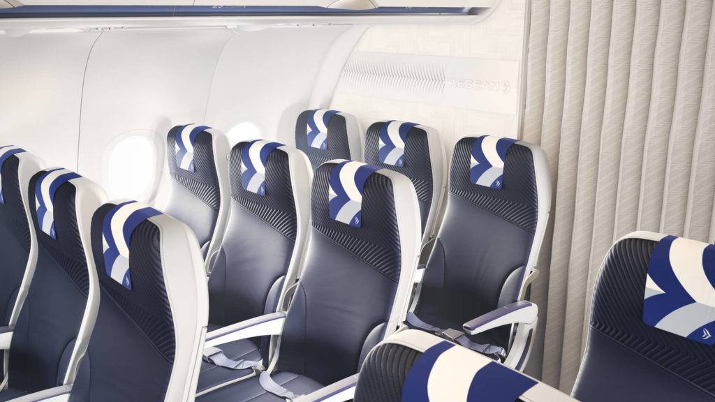 Close up of Aegean Airlines Neo aircraft cabin interior, showing a 3D brand panel on the bulkhead and intricate patterns on seat backs and curtains