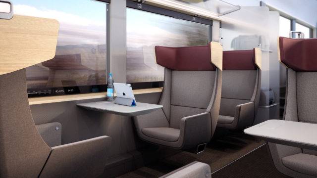 A first class train carriage. A small table features between two seats facnig one another. A tablet and water bottle are placed on the table. Large windows feature on the side