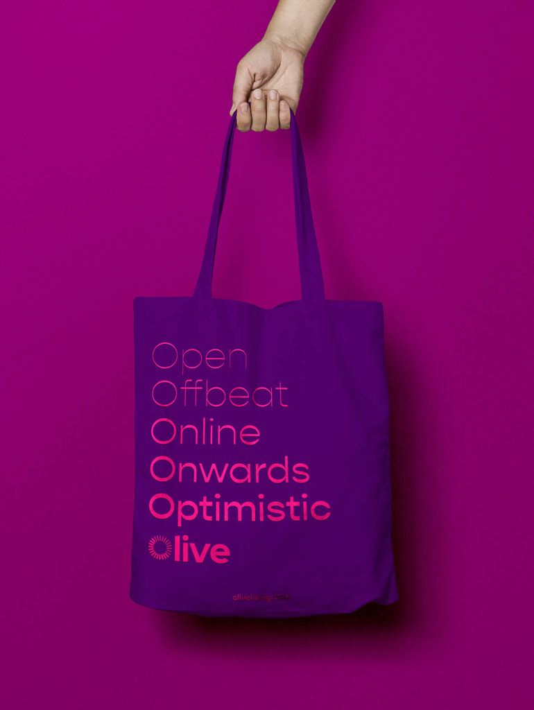 Open, offbeat, online, onwards, optimistic, olive. A hand holds a purple tote bags with those words written in pink
