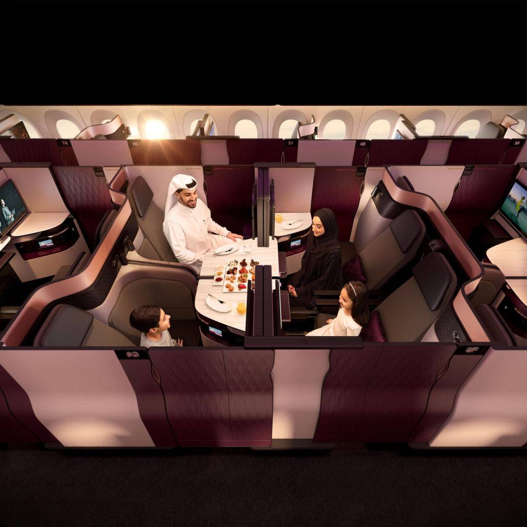 A family eats dinner together in the QSuite Business Class cabin. Four seats facing each other and a removable panel allow this unique social setting