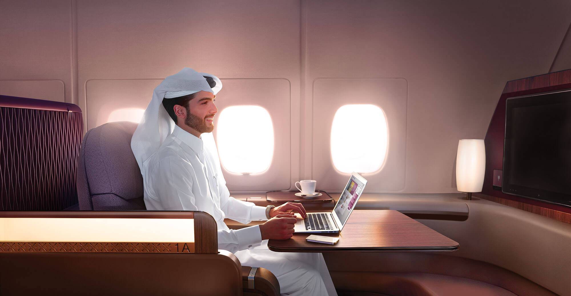 A passenger working at his laptop at a large table in the Qatar Airways A380 First Class seat