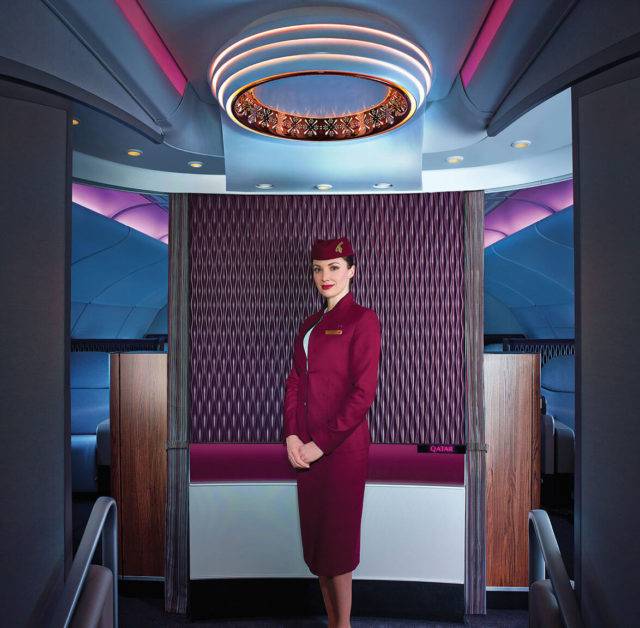 A cabin crew stands in the entrance area to Qatar Airways A380 First Class cabin, with a statement light and feature brand panel
