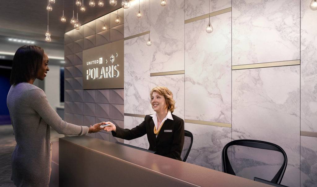 A passenger is greeted by a receptionist at the entrance to the United Polaris lounge. A marbled wall and 3D branded panel feature in the backdrop
