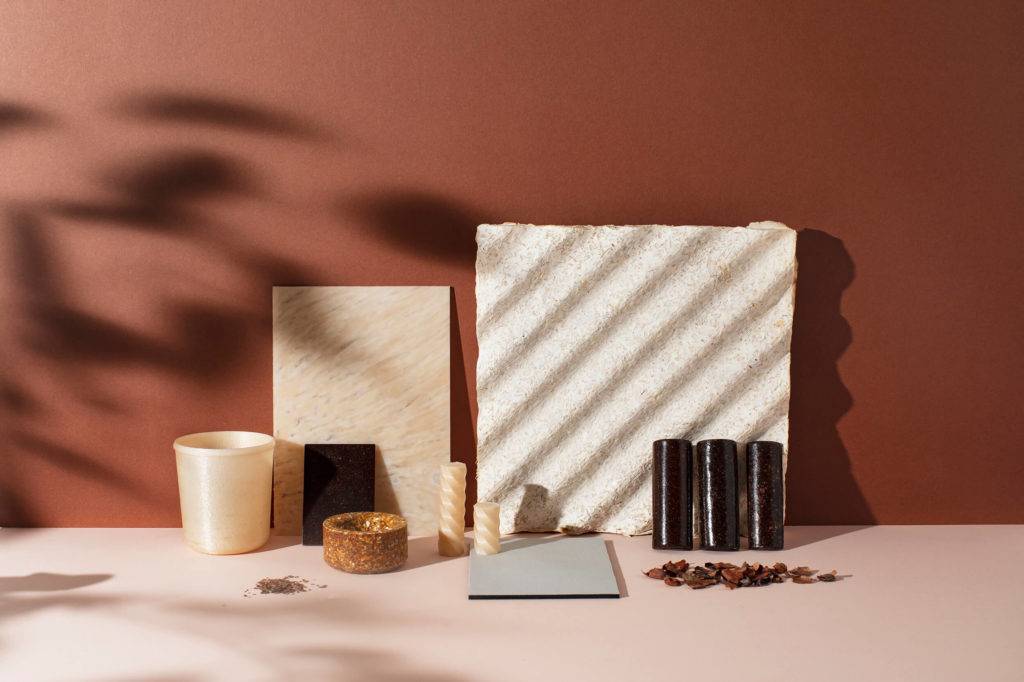 Material samples on a light pink table against a terracotta backdrop. Shadows of branches are seen on the left