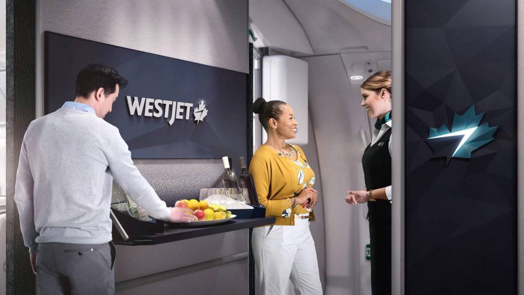 A passenger helping himself to fruit at a self-service bar while another speaks to cabin crew