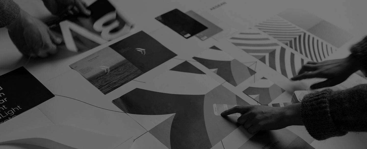 Black and white image of hands pointing at different print outs laid out, showing the new Aegean Airlines brand elements, including logo, patterns and colours