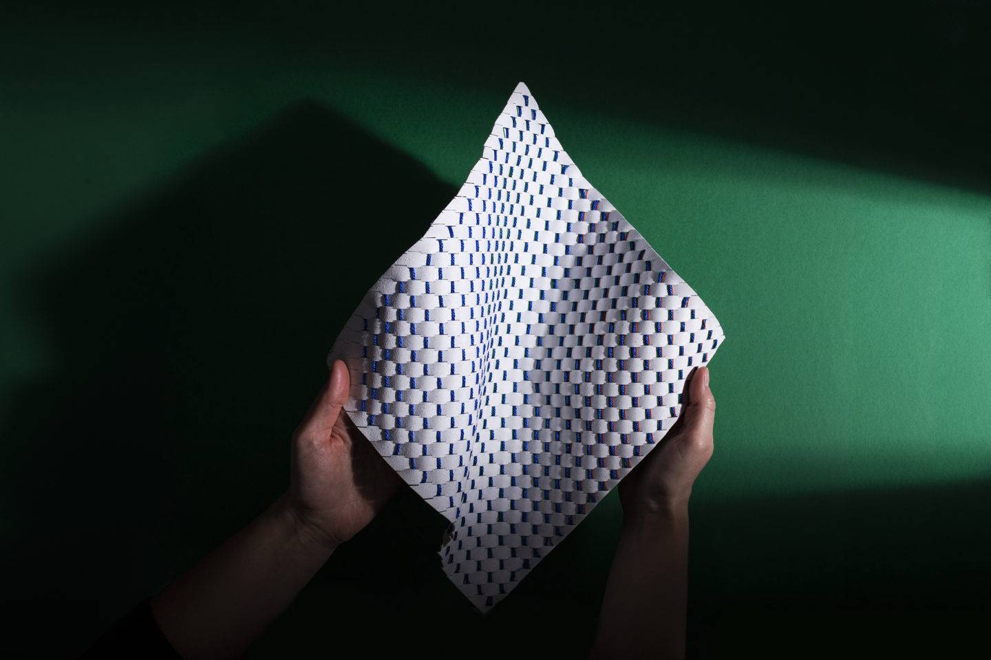 Two hands holding a white woven material in front of a dark green background