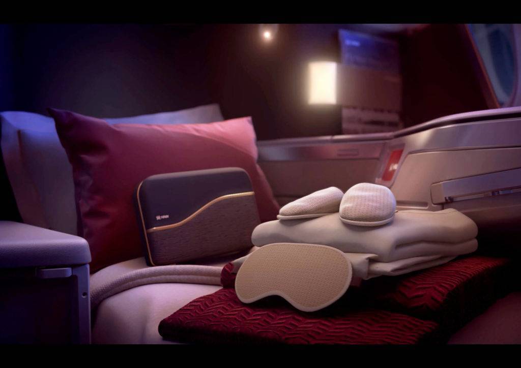 Sleep items including a sleeping mask, pyjamas and slippers are neatly placed on top of a business class airline seat in bed mode