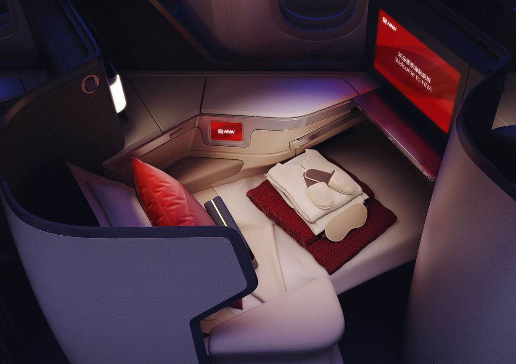 Sleep items including a sleeping mask, pyjamas and slippers are neatly placed on top of a business class airline seat in bed mode