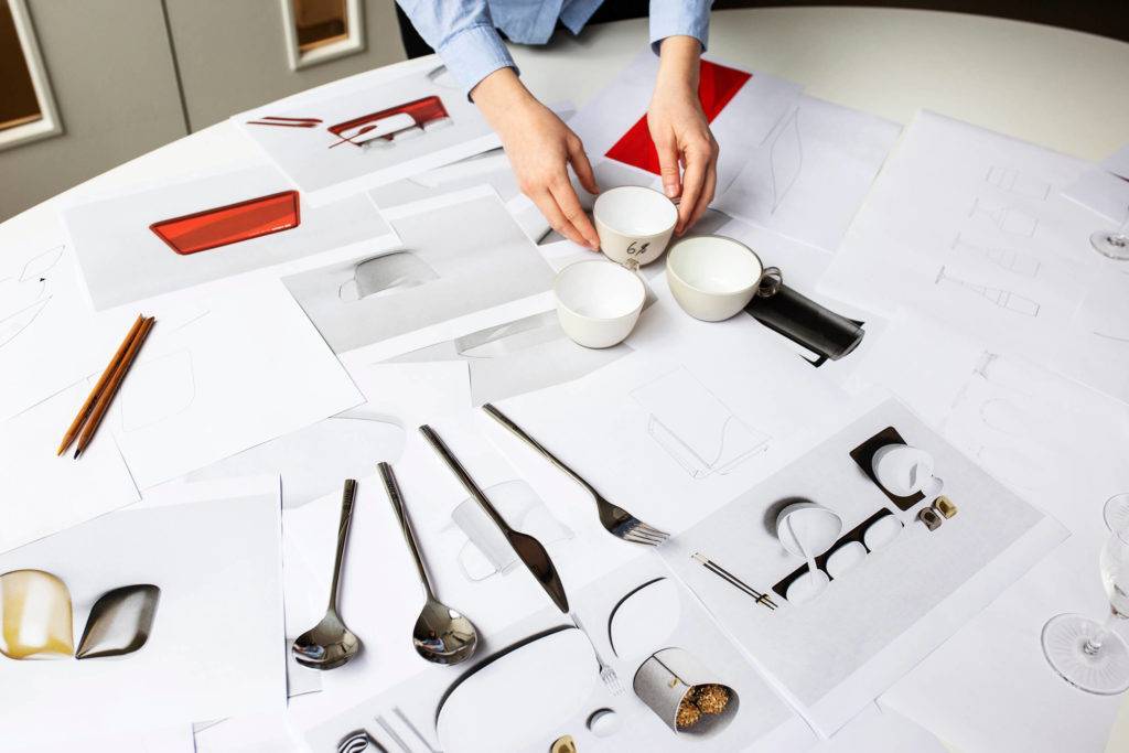 A selection of drawings as well as crockery and utensils is laid out on a table