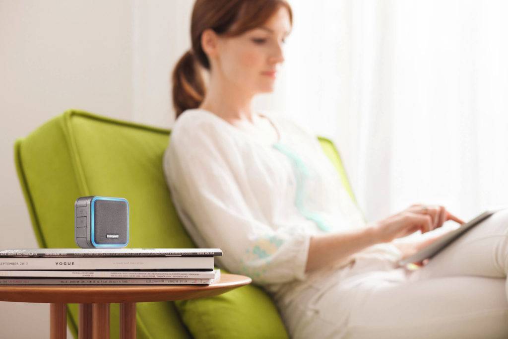 Small portable doorbell on a pile of magazines on a side table. A woman sits in a lounge chair in the background