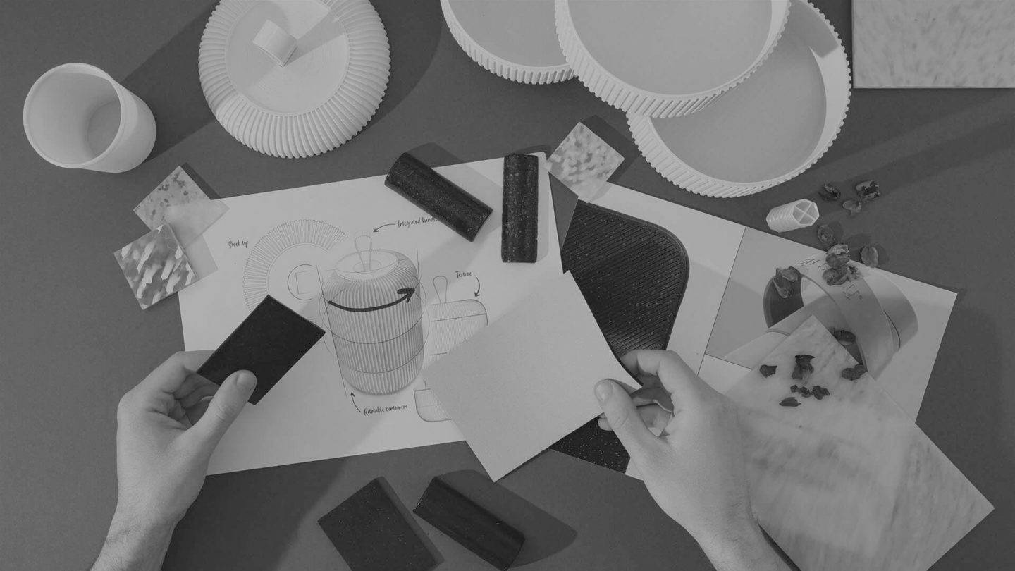 Black and white image of two hands holding colour samples over a series of sketches, material samples and 3D models