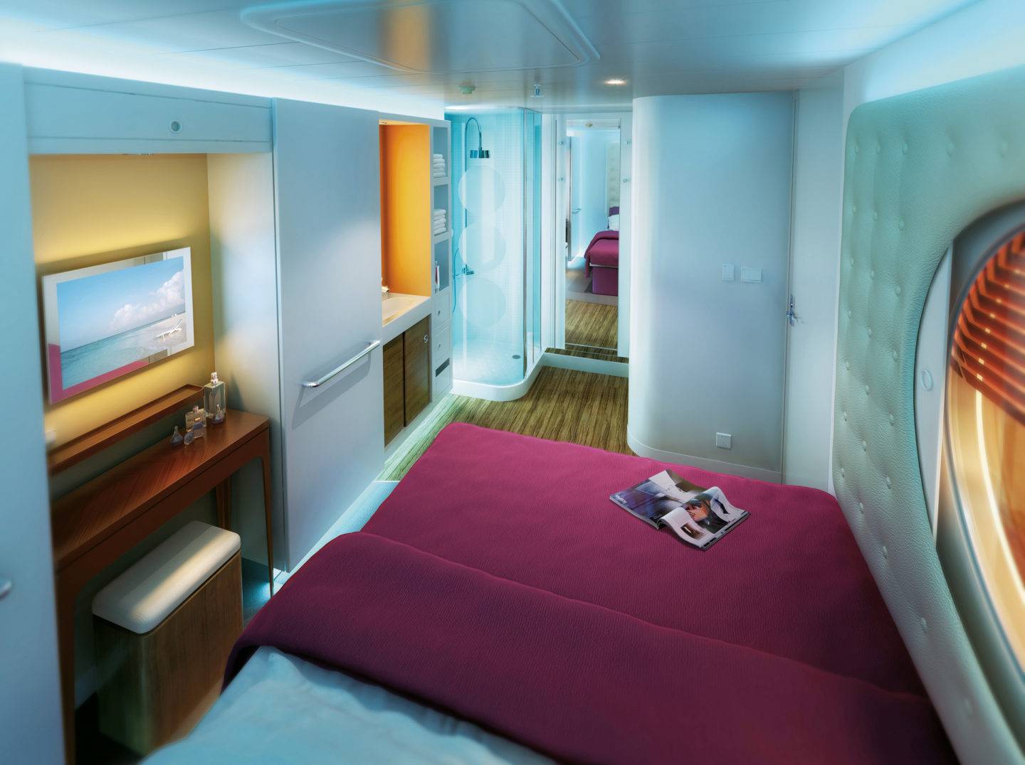 A small compact stateroom featuring a double bed, in a recessed space is a tv, and a narrow table with a stoor, a padded wall on one side has a large circular window. A sink and shower can be seen in the back of the room
