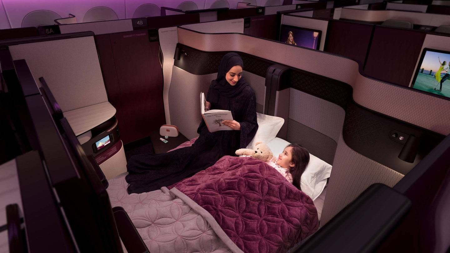 A woman reads to her daughter in the double bed configuration of the QSuite. A removable panel allows two center seats to come together to form one large double bed