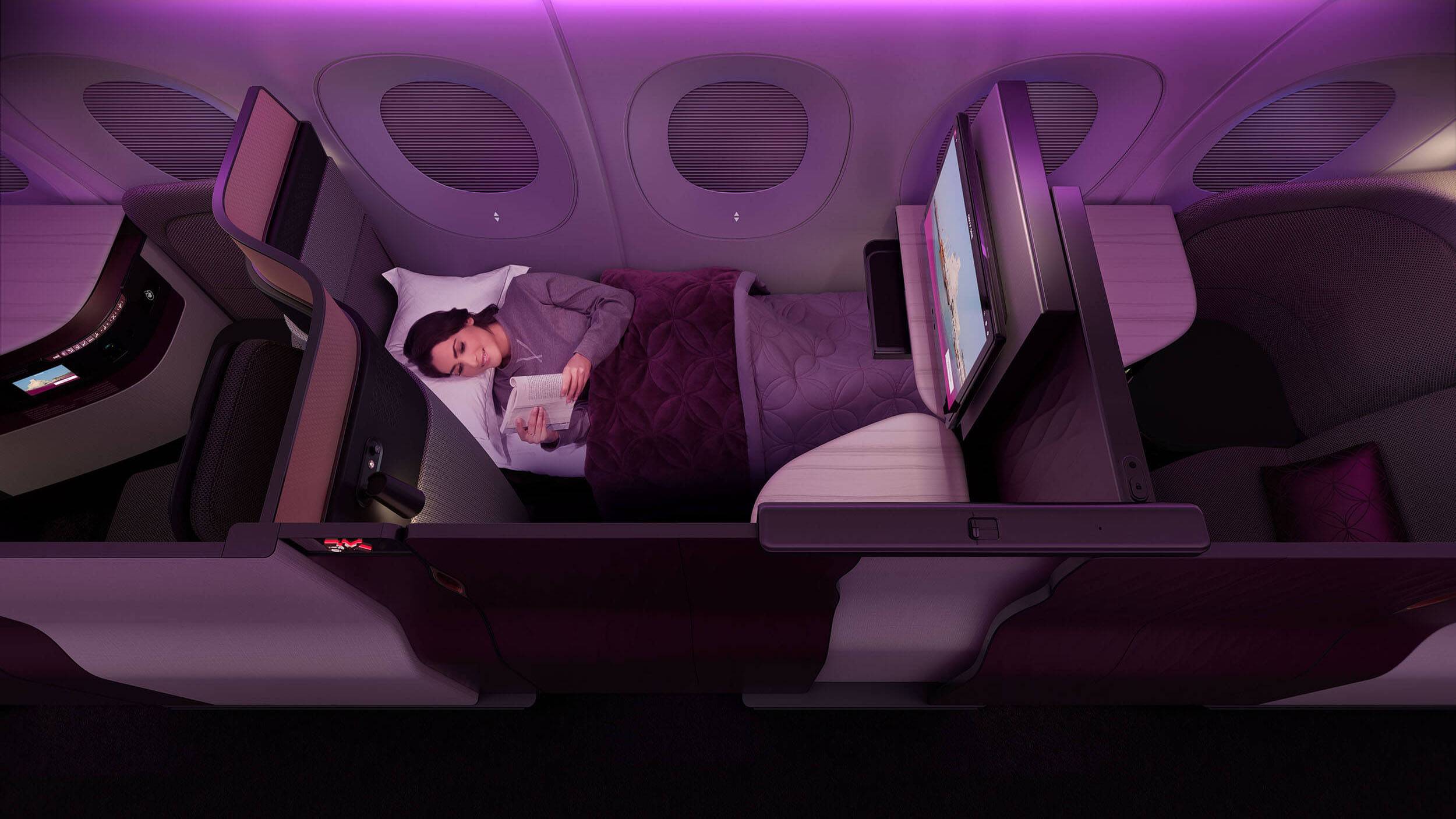 A woman lying down reading in the QSuite Business Class seat in bed mode