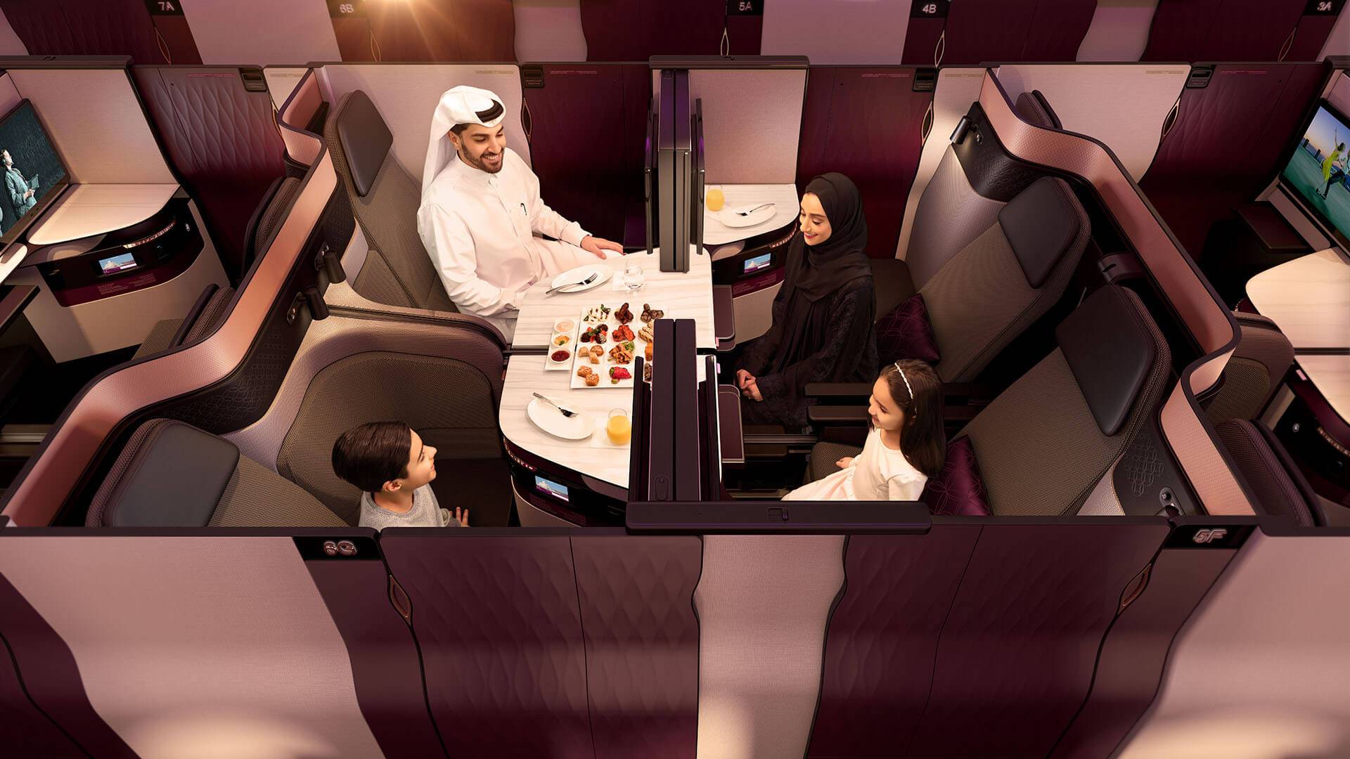 A family eats dinner together in the QSuite Business Class cabin. Four seats facing each other and a removable panel allow this unique social setting