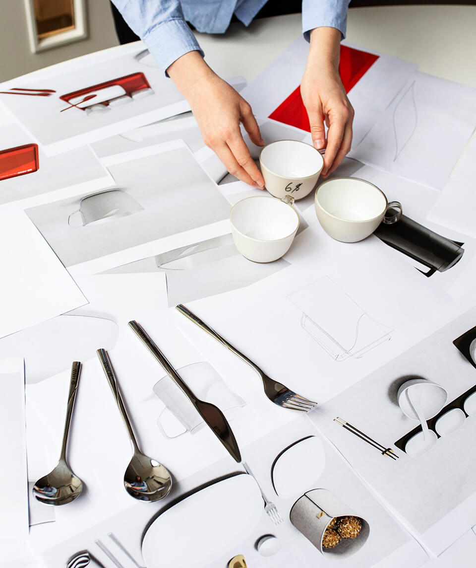 A selection of drawings as well as crockery and utensils is laid out on a table