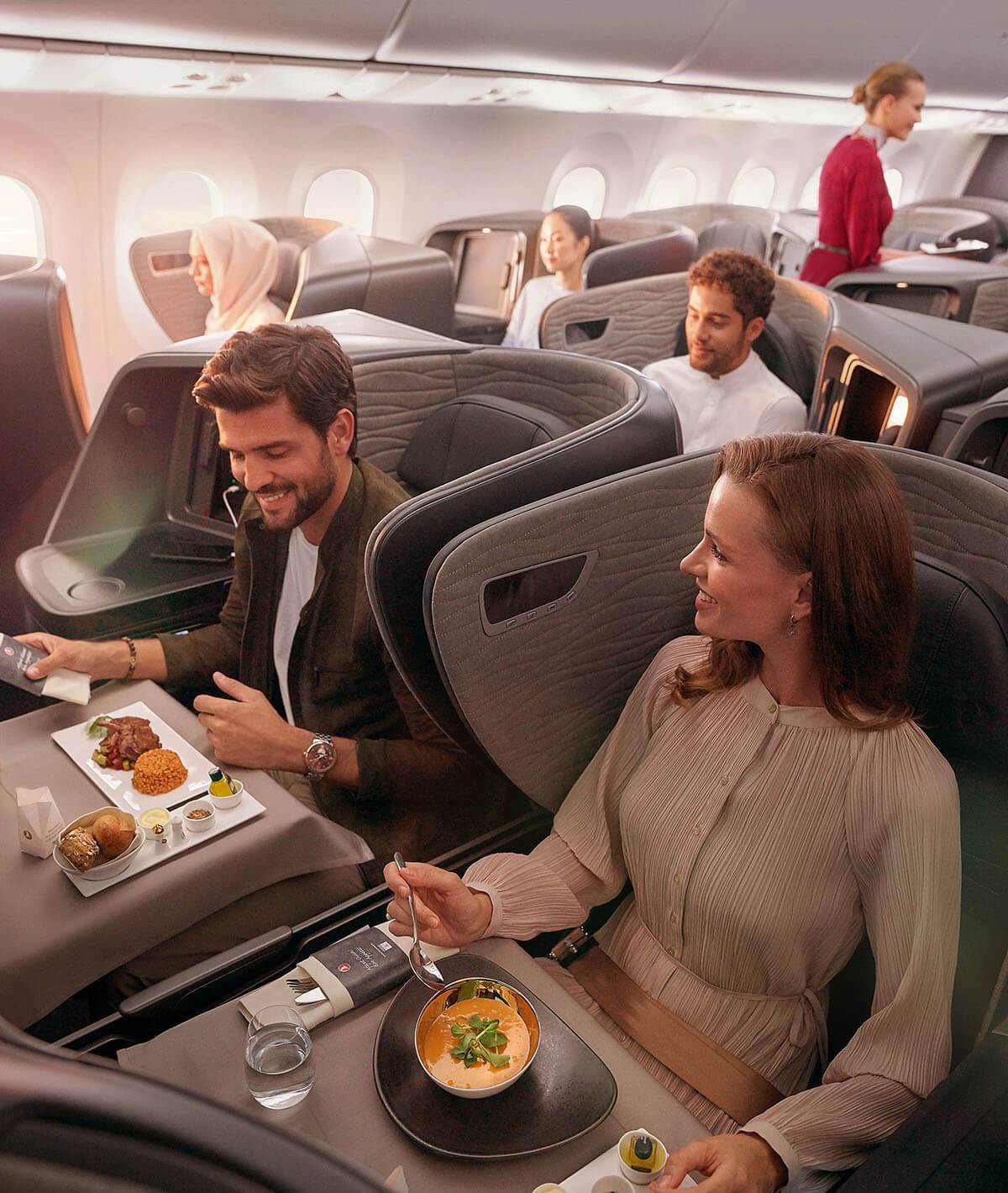 Business class cabin showing passengers enjoy the meal service, while a cabin crew serves a passenger