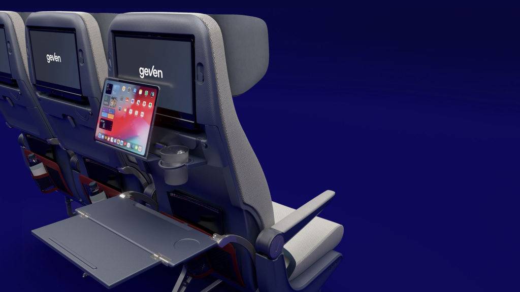 Back of an aircraft seat showing tray tables, an entertainment screen and a tablet holder