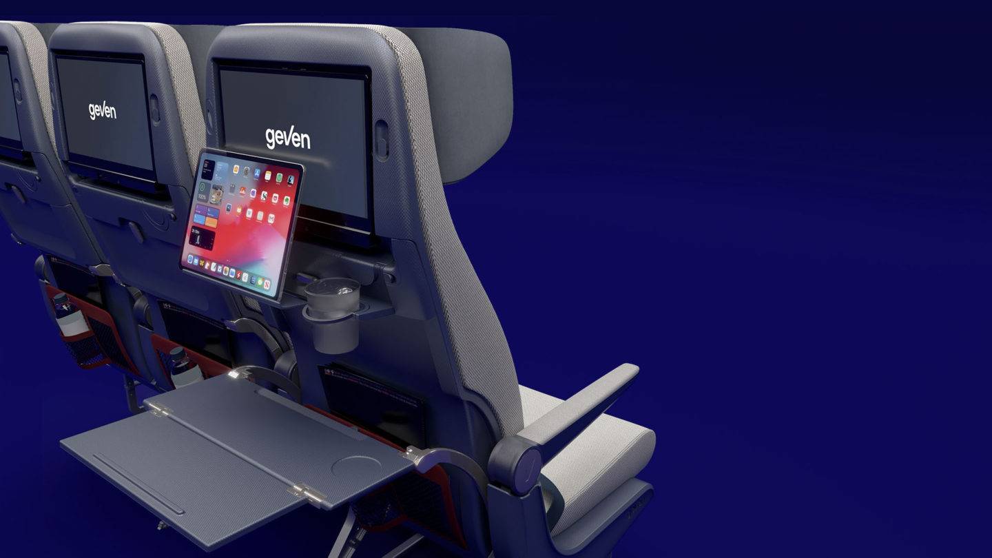 Back of an aircraft seat showing tray tables, an entertainment screen and a tablet holder