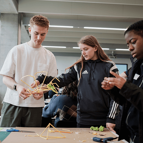 Cropped image of students and PG member working on a design made from straws